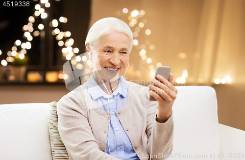 Image of senior woman with smartphone and earphones on xmas