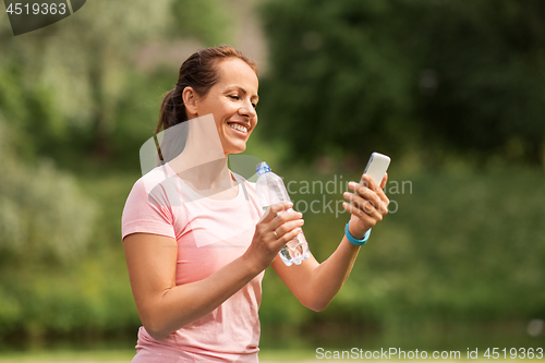 Image of woman with smartphone drinking water in park