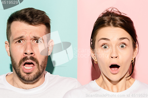 Image of Closeup portrait of young couple, man, woman. One being excited happy smiling, other serious, concerned, unhappy on pink and blue background. Emotion contrasts