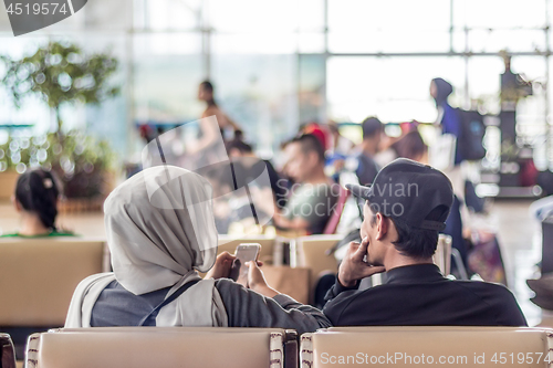 Image of Modern muslim islamic asian couple using their smartphone apps while sitting and waiting for flight departure at international airport terminal