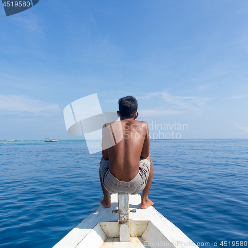 Image of Local Sporty Guy Sitting Topless at the Bow of Traditional White Wooden Sail Boat, Looking At Beautiful Blue Sea of Gili Islands near Bali, Indonesia