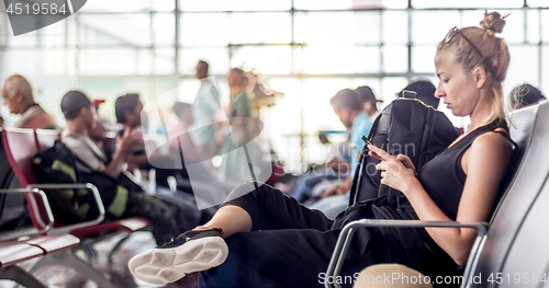 Image of Female traveler using her cell phone while waiting to board a plane at departure gates at asian airport terminal.