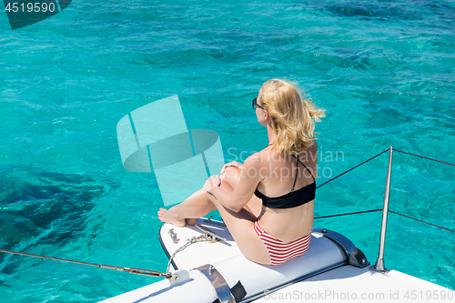 Image of Woman relaxing on a summer sailing cruise, sitting on a luxury catamaran near picture perfect white sandy beach on Spargi island in Maddalena Archipelago, Sardinia, Italy.