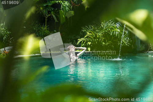 Image of Sensual young woman relaxing in outdoor spa infinity swimming pool surrounded with lush tropical greenery of Ubud, Bali.