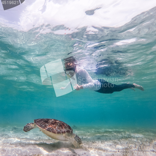 Image of Woman on vacations wearing snokeling mask swimming with sea turtle in turquoise blue water of Gili islands, Indonesia. Underwater photo.