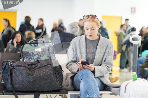 Image of Female traveler reading on her cell phone while waiting to board a plane at departure gates at airport terminal.