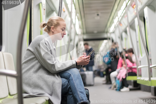 Image of Beautiful blonde woman wearing winter coat reading on the phone while traveling by metro public transport.