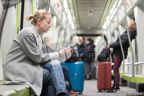 Image of Beautiful blonde woman wearing winter coat reading on the phone while traveling by metro public transport.