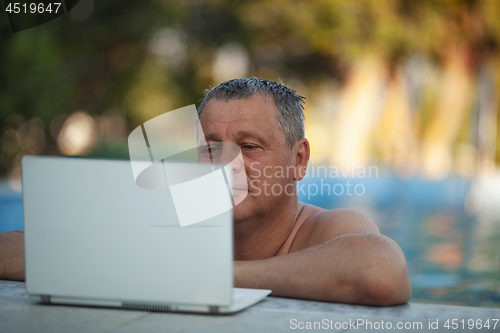 Image of A middle aged man in the swimming pool watching something on a laptop