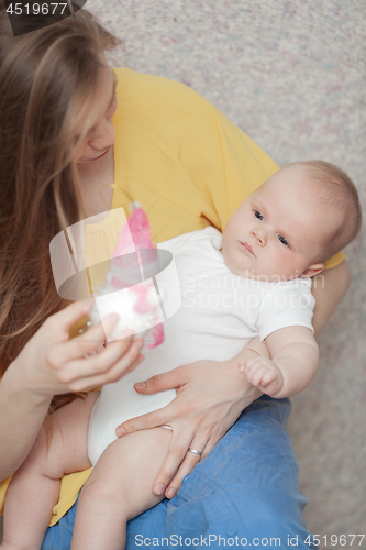 Image of A baby boy in arms of a long haired woman looking at a toy in her hand