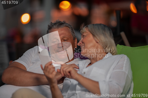 Image of Cheerful mature couple relaxing outdoor and looking through the mobile photos