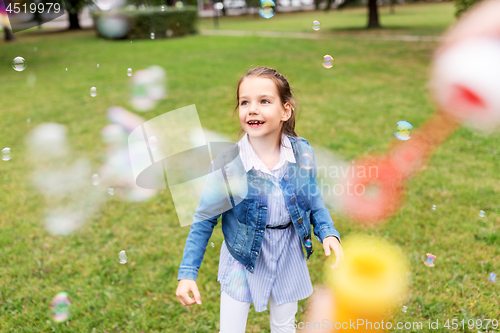 Image of happy girl playing with soap bubbles at park