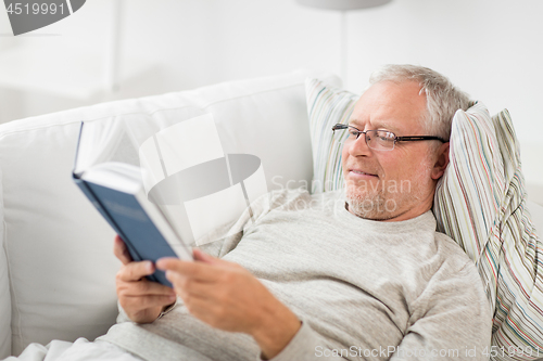 Image of senior man lying on sofa and reading book at home