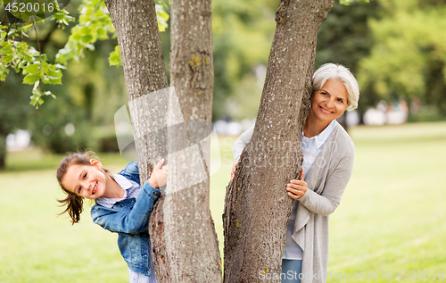 Image of grandmother and granddaughter behind tree at park