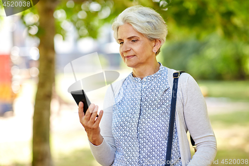 Image of happy senior woman with smartphone at summer park