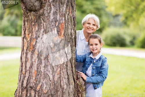 Image of grandmother and granddaughter behind tree at park