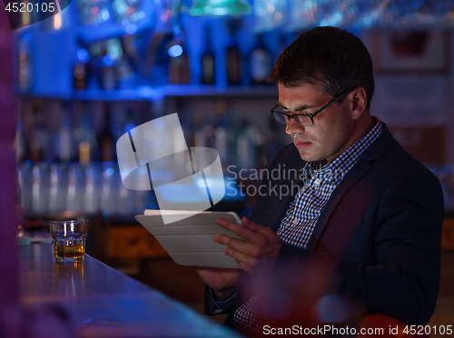 Image of Businessman with tablet pc and whisky at the bar counter