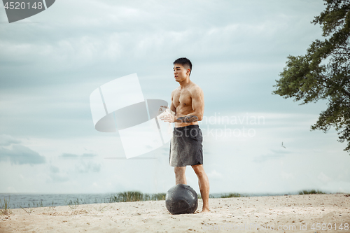 Image of Young healthy man athlete doing squats at the beach