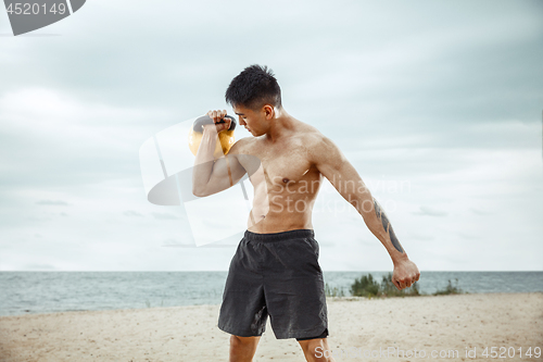 Image of Young healthy man athlete doing squats at the beach