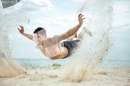 Image of Young healthy man athlete doing squats at the beach