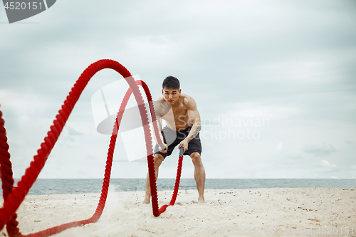 Image of Young healthy man athlete doing squats at the beach