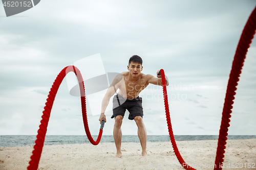 Image of Young healthy man athlete doing squats at the beach