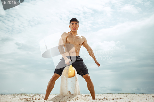 Image of Young healthy man athlete doing squats at the beach