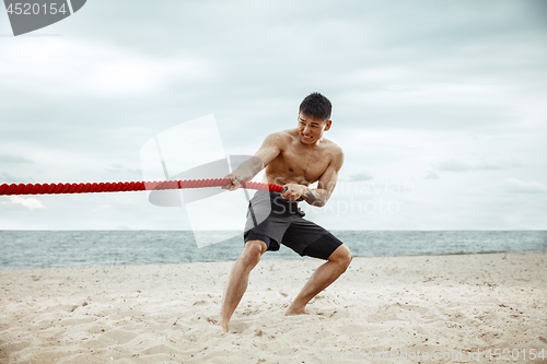 Image of Young healthy man athlete doing squats at the beach