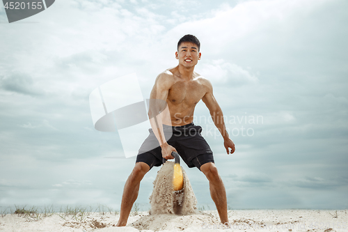 Image of Young healthy man athlete doing squats at the beach