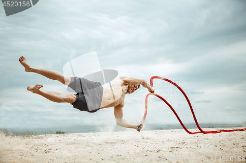 Image of Young healthy man athlete doing squats at the beach