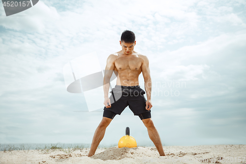 Image of Young healthy man athlete doing squats at the beach