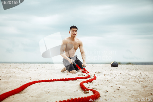 Image of Young healthy man athlete doing squats at the beach