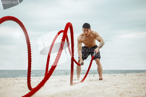 Image of Young healthy man athlete doing squats at the beach