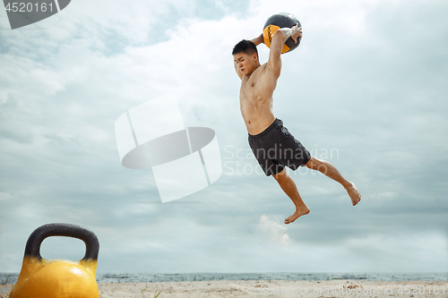 Image of Young healthy man athlete doing squats at the beach