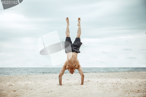 Image of Young healthy man athlete doing squats at the beach