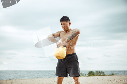 Image of Young healthy man athlete doing squats at the beach