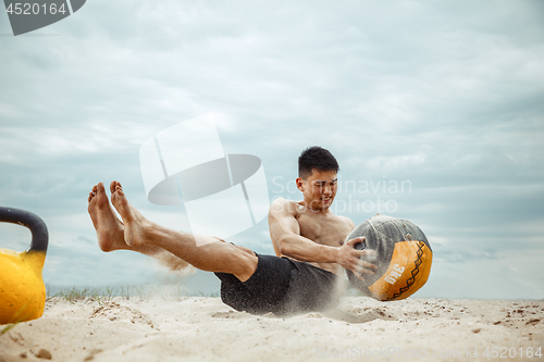 Image of Young healthy man athlete doing squats at the beach