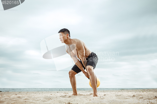 Image of Young healthy man athlete doing squats at the beach