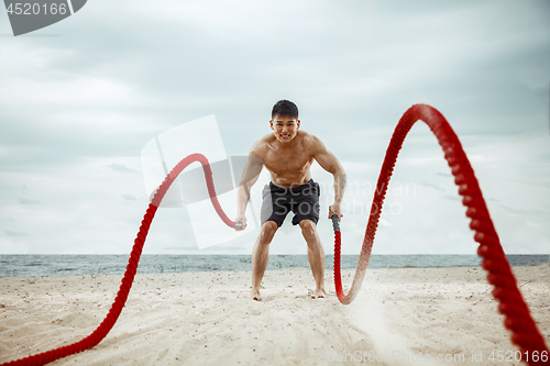 Image of Young healthy man athlete doing squats at the beach