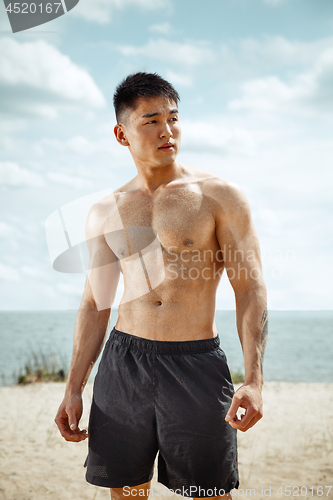 Image of Young healthy man athlete doing squats at the beach