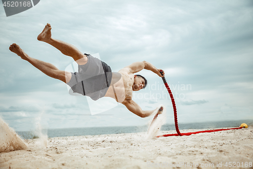 Image of Young healthy man athlete doing squats at the beach