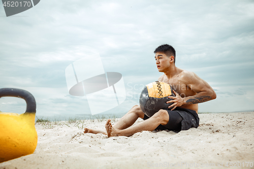 Image of Young healthy man athlete doing squats at the beach