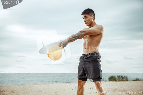 Image of Young healthy man athlete doing squats at the beach