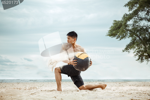 Image of Young healthy man athlete doing squats at the beach