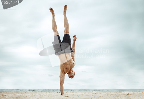 Image of Young healthy man athlete doing squats at the beach