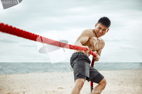 Image of Young healthy man athlete doing squats at the beach