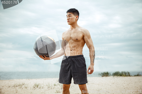 Image of Young healthy man athlete doing squats at the beach