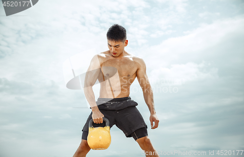 Image of Young healthy man athlete doing squats at the beach