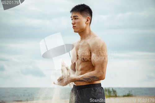 Image of Young healthy man athlete doing squats at the beach