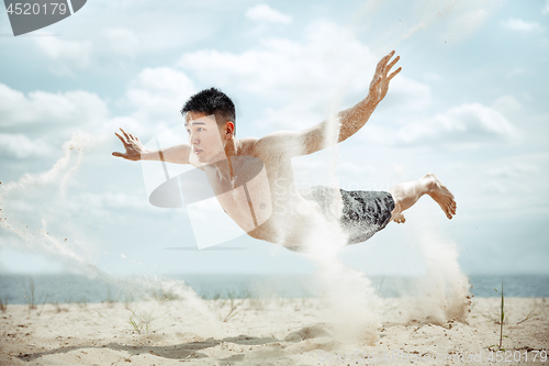 Image of Young healthy man athlete doing squats at the beach